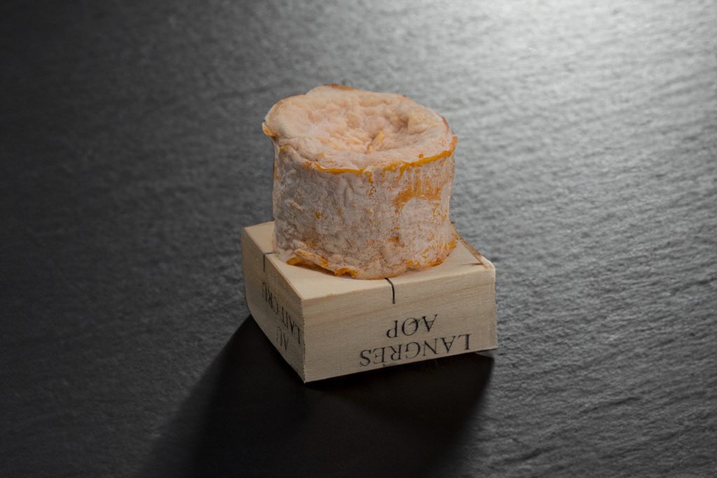 Langres fermier à croûte orangée posé sur sa boîte en bois